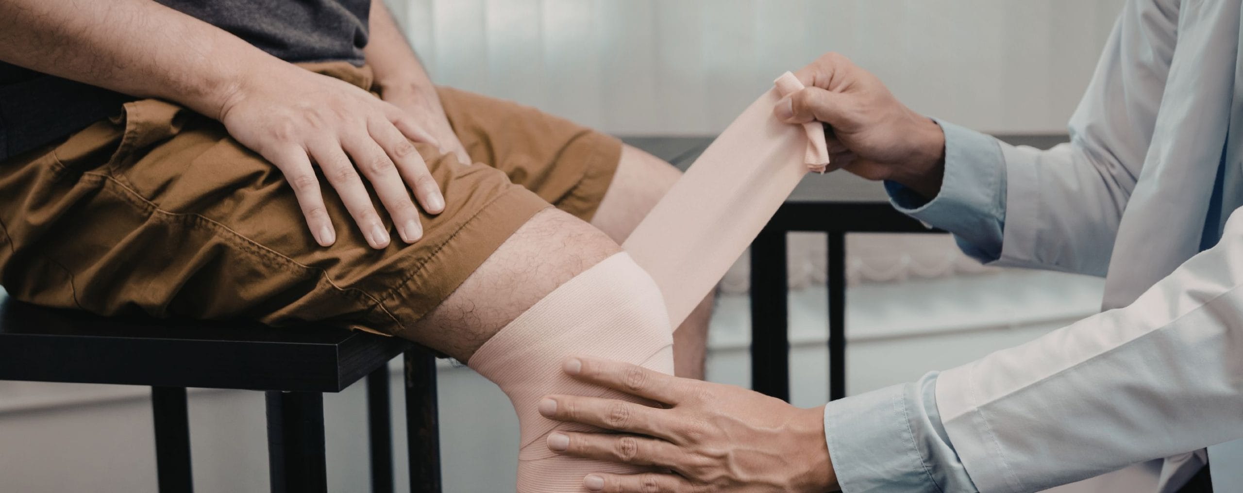 Physiotherapist wrapping an elastic bandage to the athlete’s ACL injury during rehab