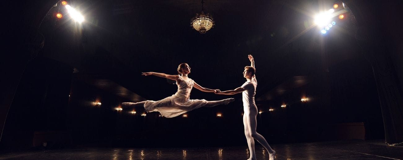 Two ballet dancers performing on a darkened stage under spotlights, representing hypermobility in dancers and performing artists