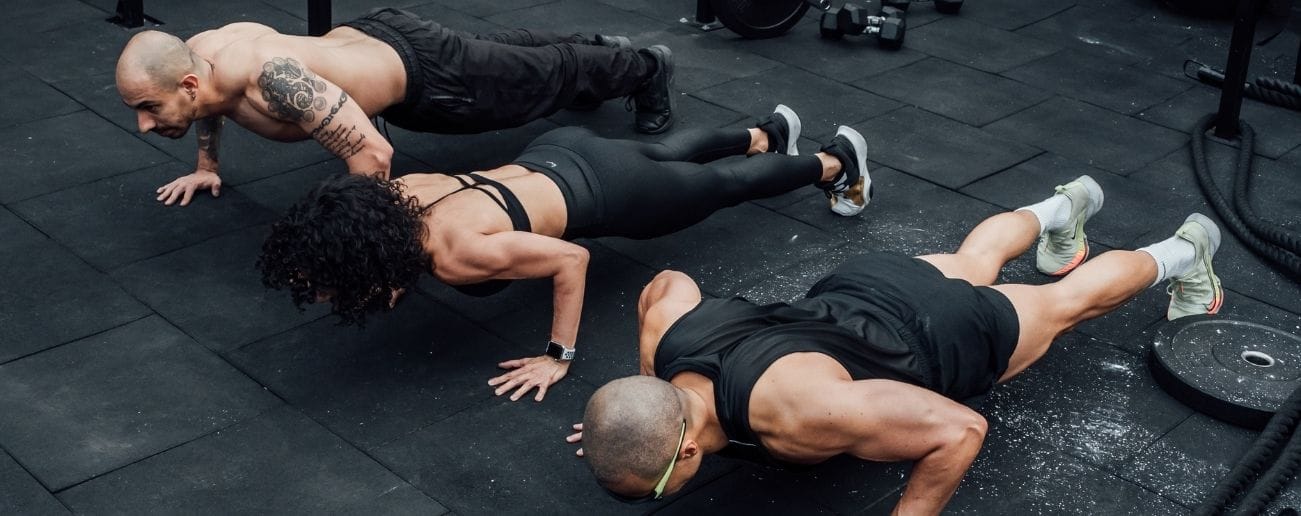 Group of athletes performing synchronised burpees on a gym floor during a Hyrox-style training session