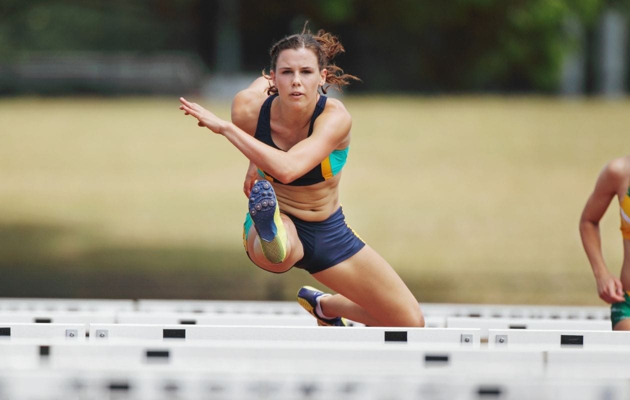 Female athlete clearing a hurdle on an athletics track, demonstrating a confident return to sport after ACL rehabilitation