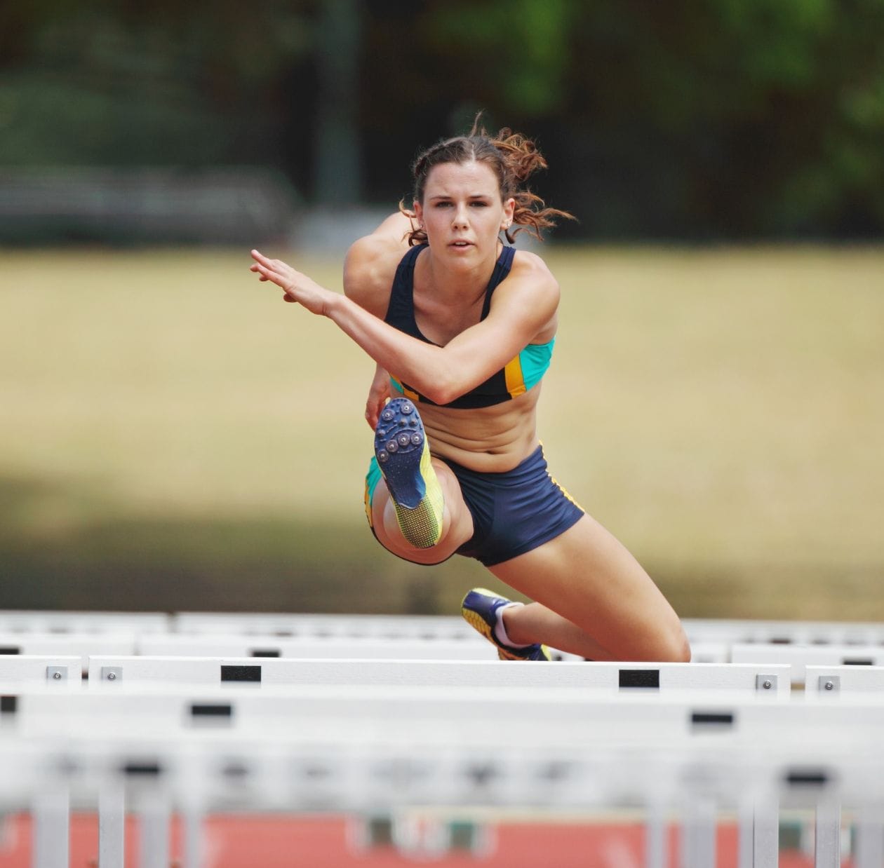 Female athlete clearing a hurdle on an athletics track, demonstrating a confident return to sport after ACL rehabilitation