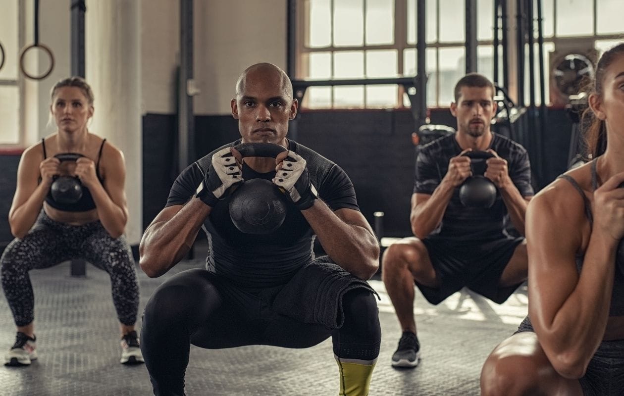 Group of CrossFit athletes performing synchronised kettlebell goblet squats during a class workout