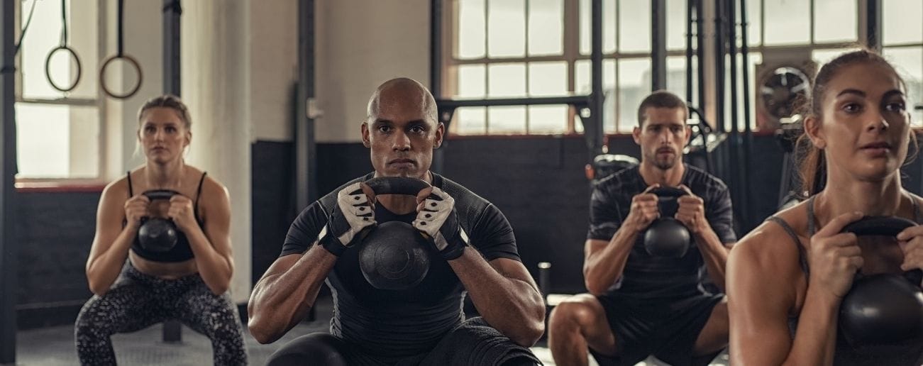 Group of CrossFit athletes performing synchronised kettlebell goblet squats during a class workout