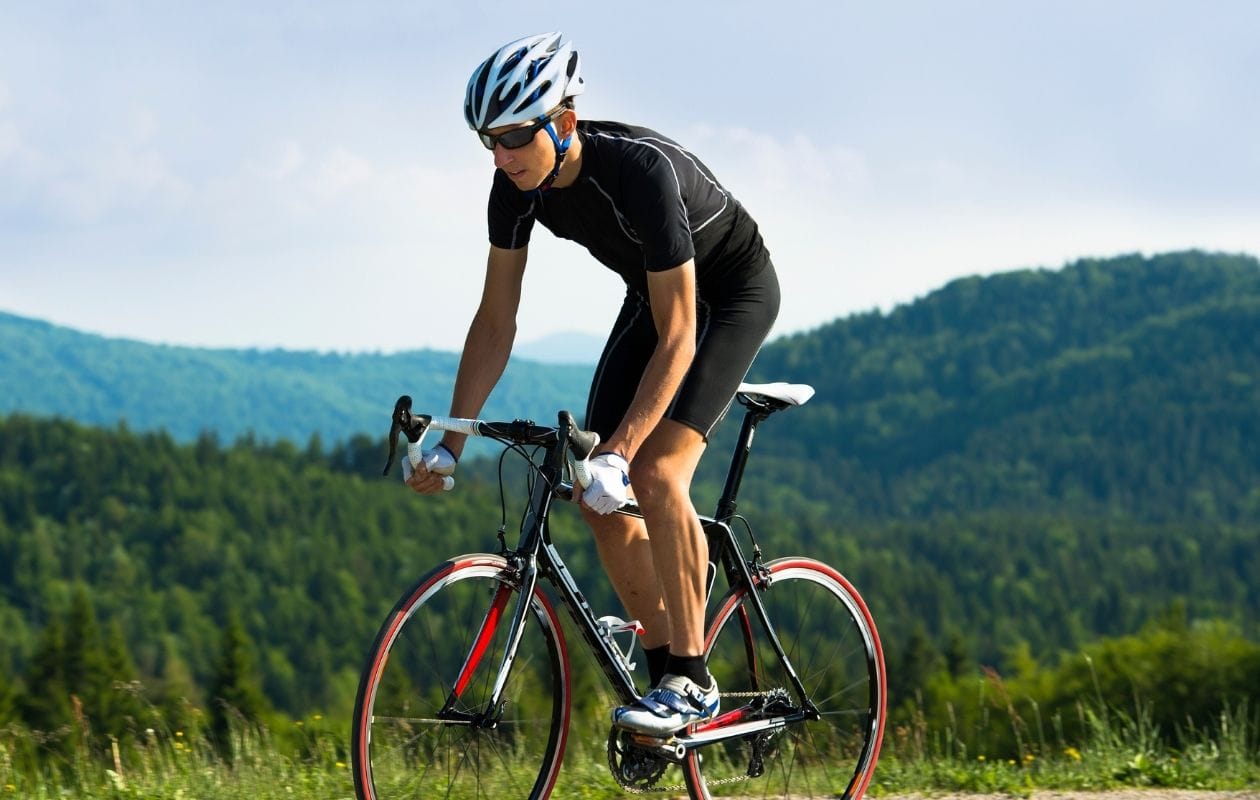 Male road cyclist riding on a country road, demonstrating a confident return to endurance sport after spine injury rehabilitation