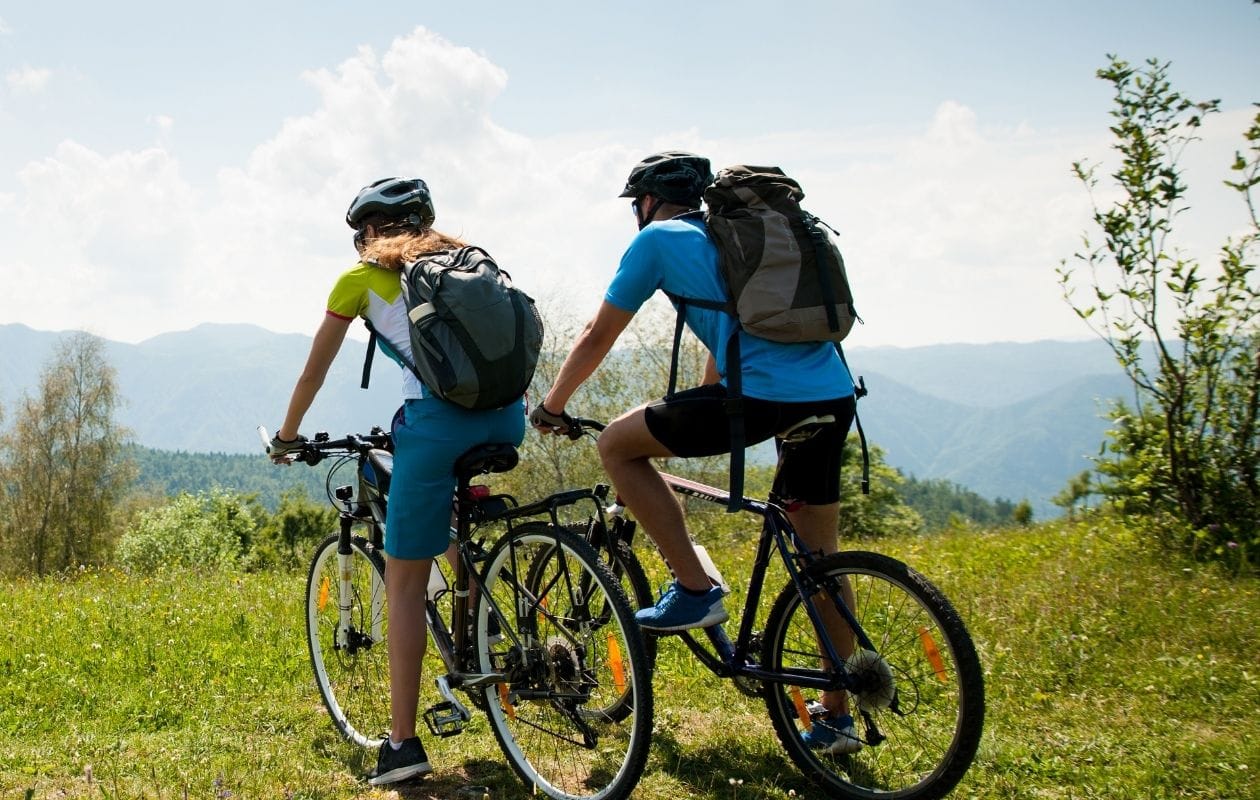 Two cyclists pausing on a mountain trail, looking out across the landscape Two cyclists pausing on a mountain trail, looking out across the landscape