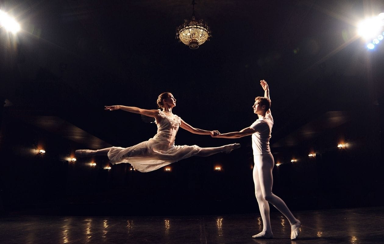 Two ballet dancers performing on a darkened stage under spotlights, representing hypermobility in dancers and performing artists