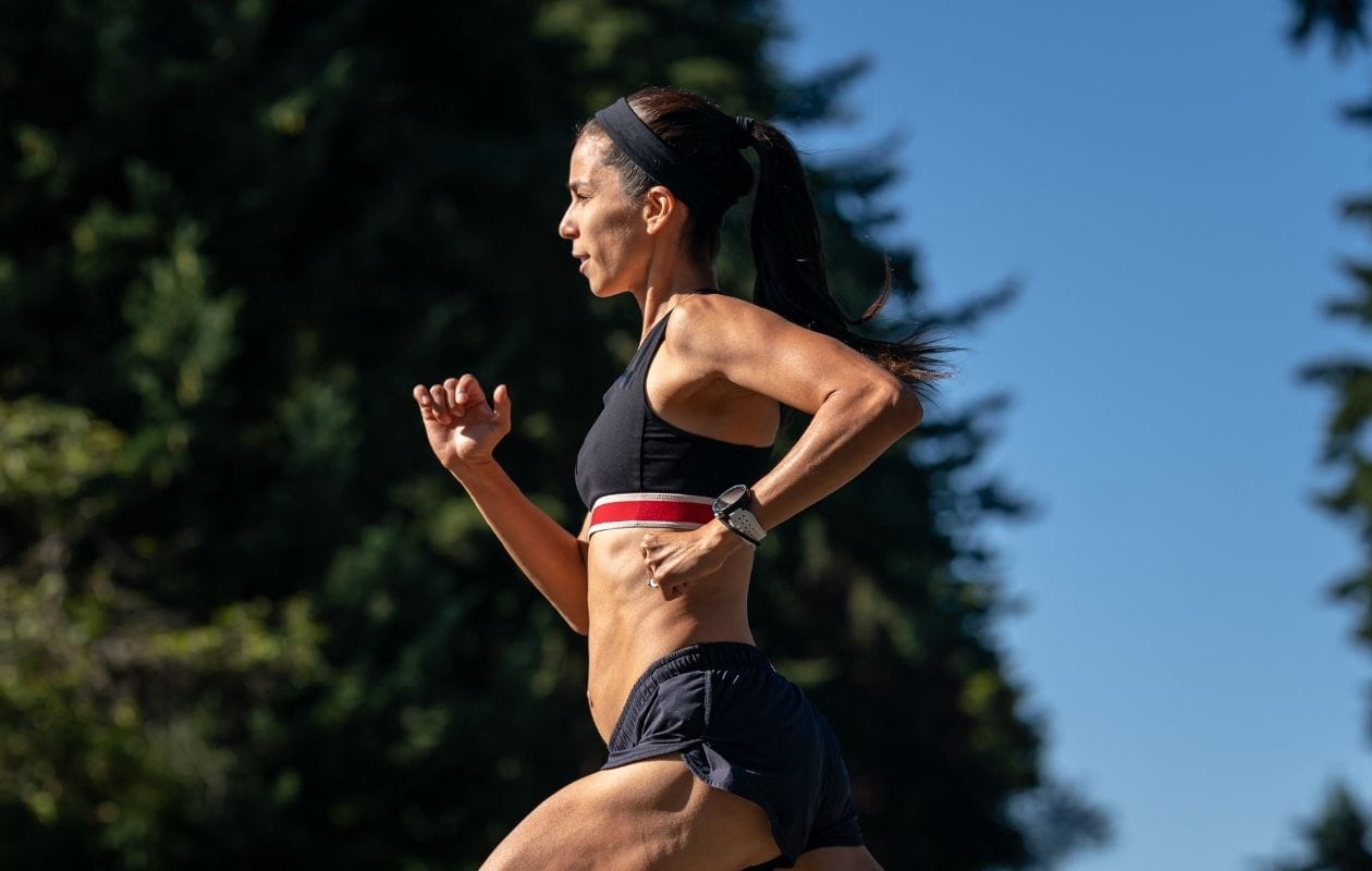 Female runner in profile running outdoors on a sunny day, demonstrating a confident return to running after foot and ankle rehabilitation
