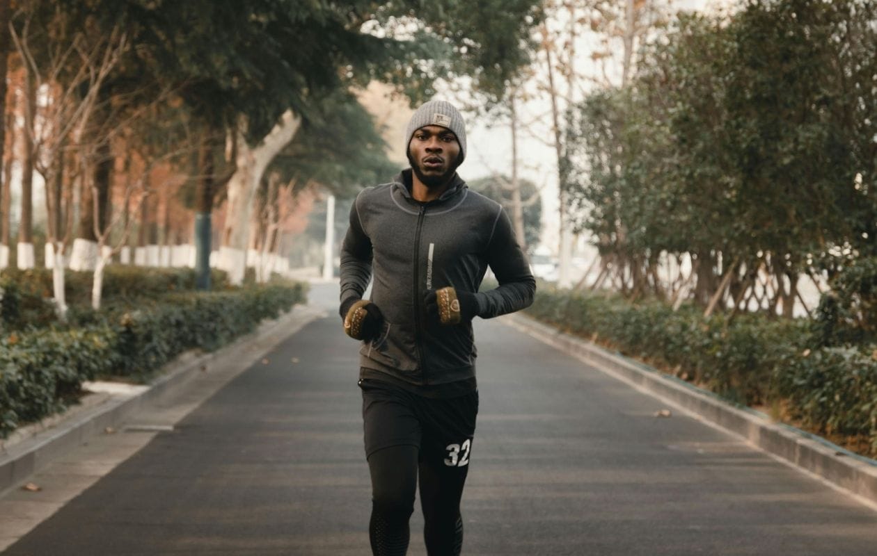 Male runner in cold-weather kit running along a tree-lined road, demonstrating a confident return to running after foot and ankle rehabilitation