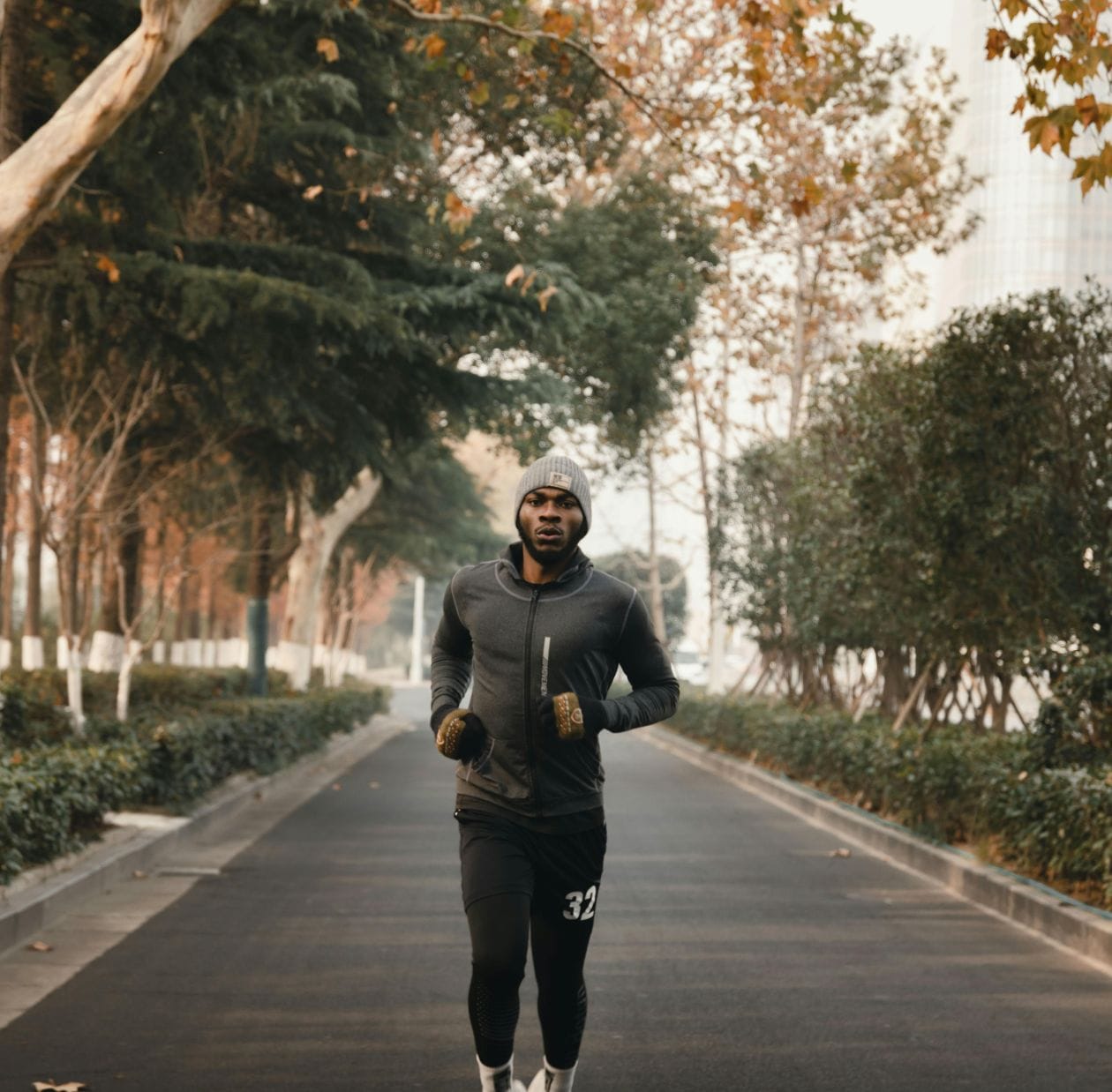 Male runner in cold-weather kit running along a tree-lined road, demonstrating a confident return to running after foot and ankle rehabilitation