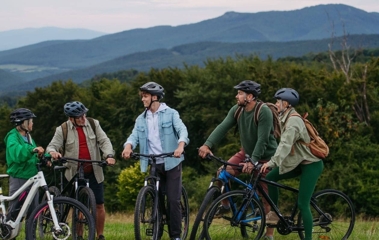 Group of recreational cyclists of mixed ages wearing helmets, pausing on bikes at a scenic mountain viewpoint
