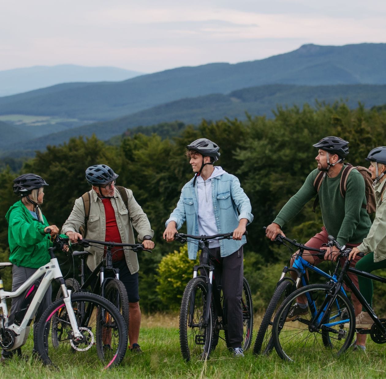 Group of recreational cyclists of mixed ages wearing helmets, pausing on bikes at a scenic mountain viewpoint