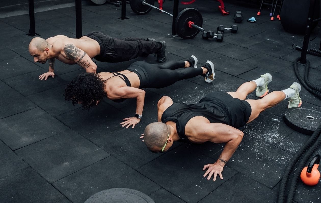 Group of athletes performing synchronised burpees on a gym floor during a Hyrox-style training session