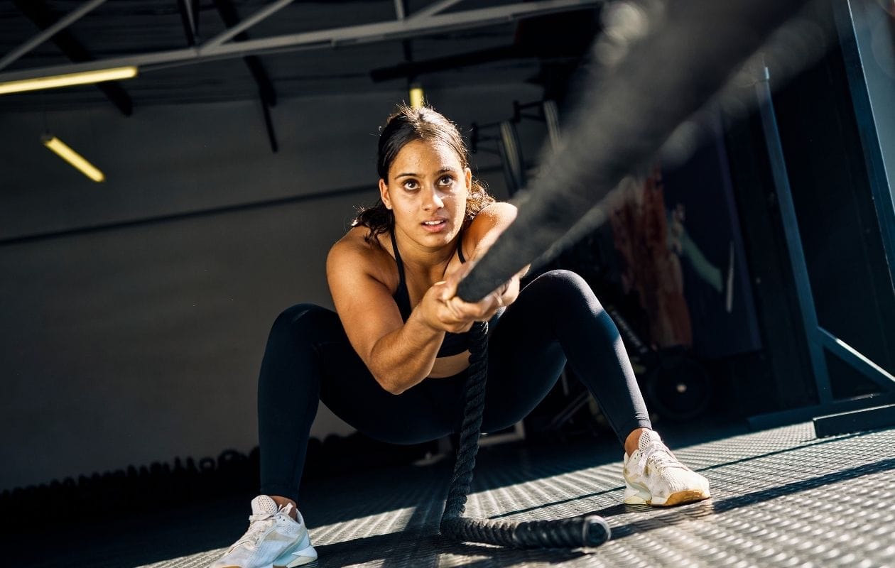 Female Hyrox athlete training with battle ropes in a gym, demonstrating functional fitness conditioning