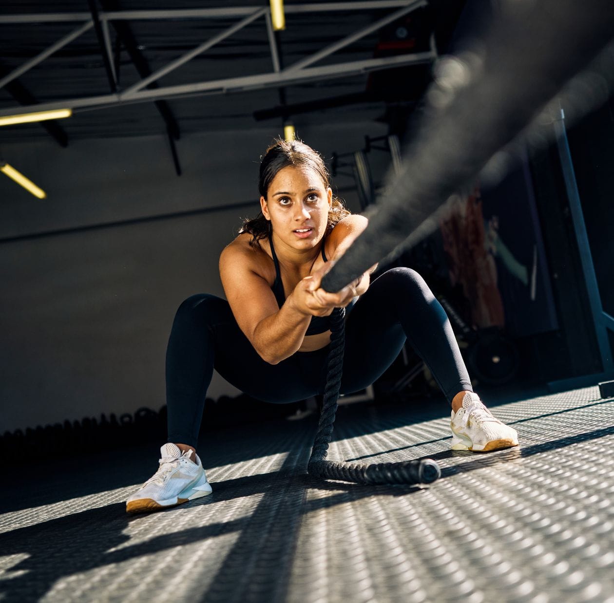 Female Hyrox athlete training with battle ropes in a gym, demonstrating functional fitness conditioning