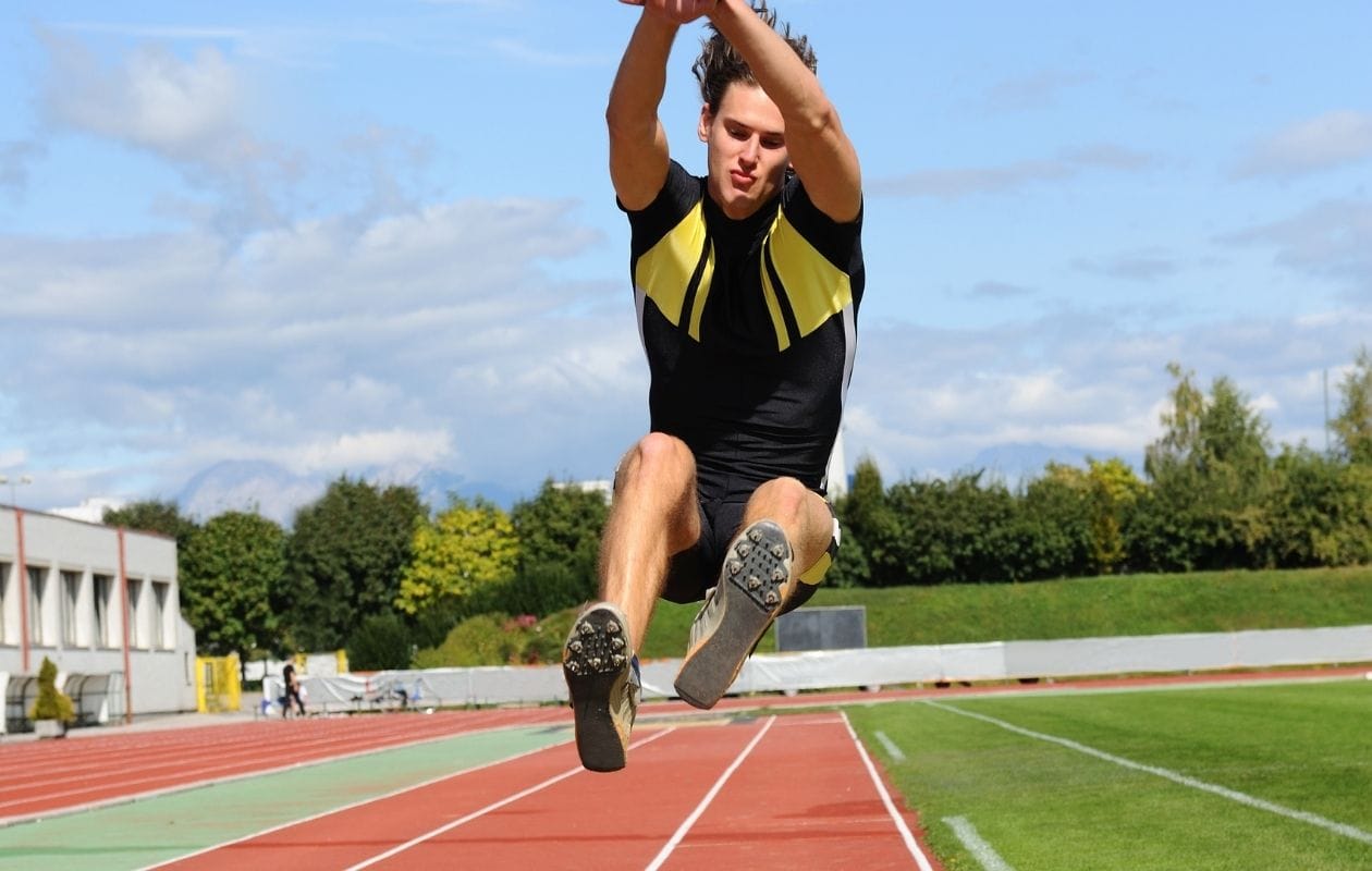 Male long jumper mid-flight above the sand pit, demonstrating a confident return to athletics after sports knee injury rehabilitation