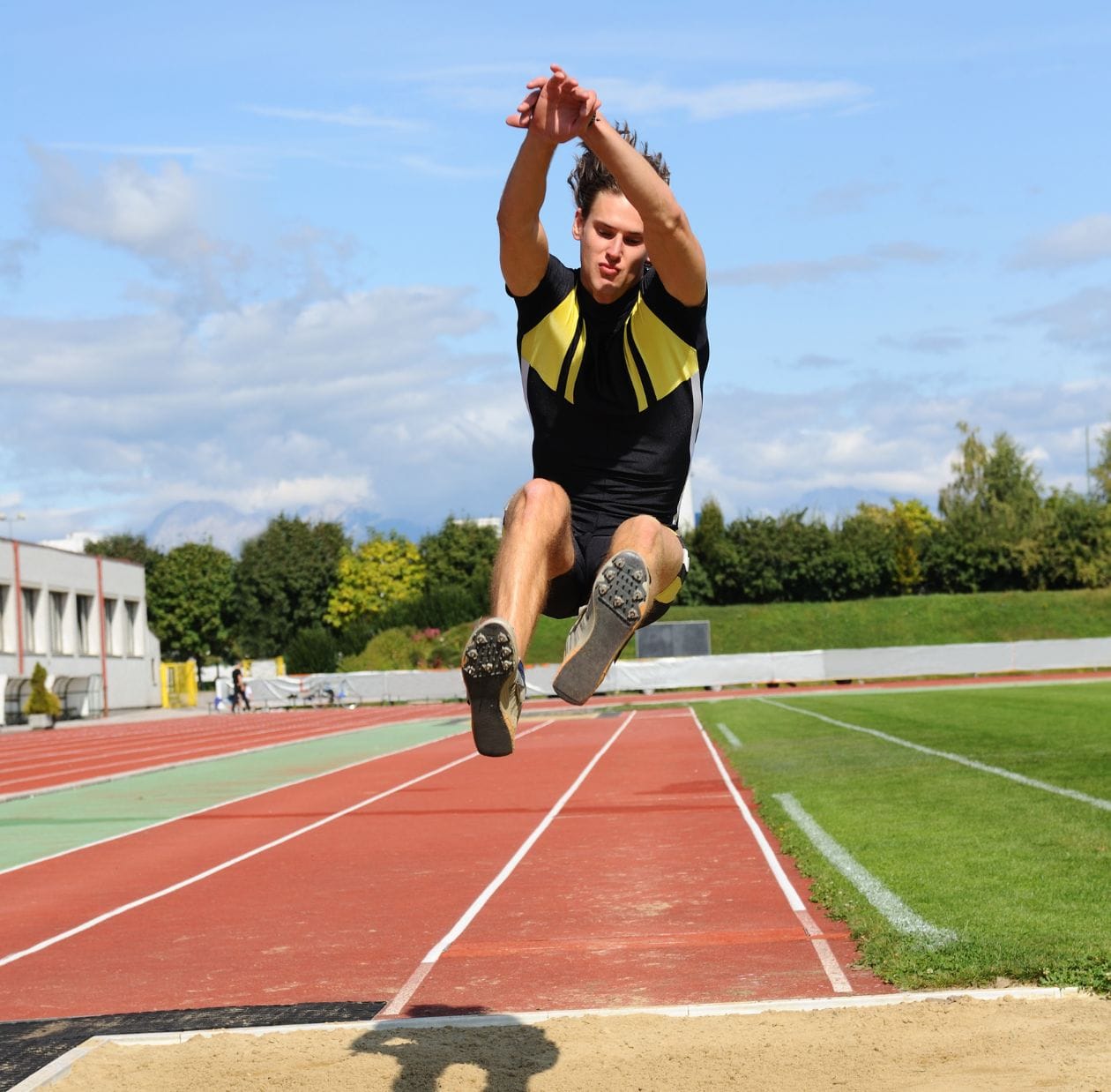 Male long jumper mid-flight above the sand pit, demonstrating a confident return to athletics after sports knee injury rehabilitation