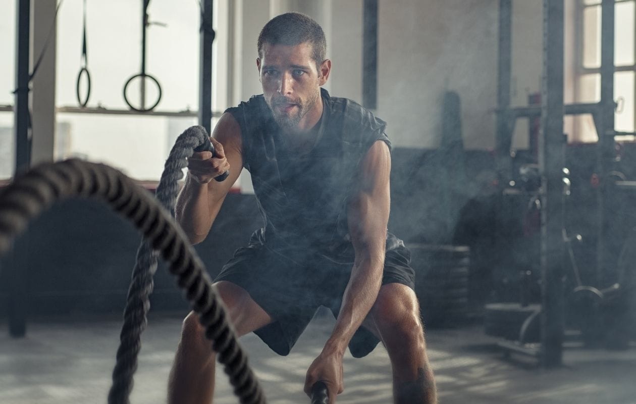 Male CrossFit athlete training with battle ropes in a gym, demonstrating high-intensity functional fitness conditioning