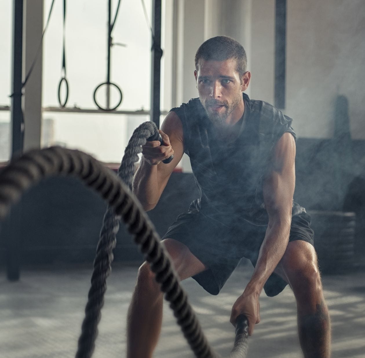 Male CrossFit athlete training with battle ropes in a gym, demonstrating high-intensity functional fitness conditioning