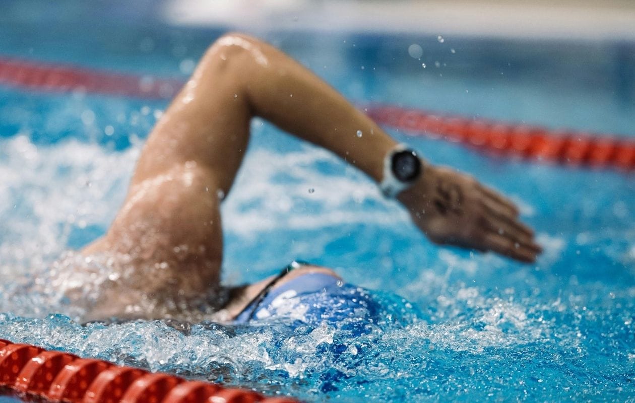 Male swimmer performing front crawl in a pool, demonstrating a confident return to overhead sport after shoulder rehabilitation